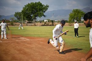 Young man runs with cricket bat, while other players look on.