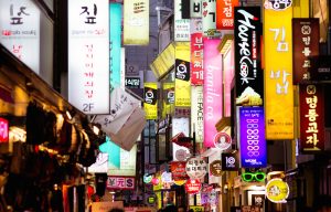 Multiple illuminated commercial signs in Seoul street at dusk