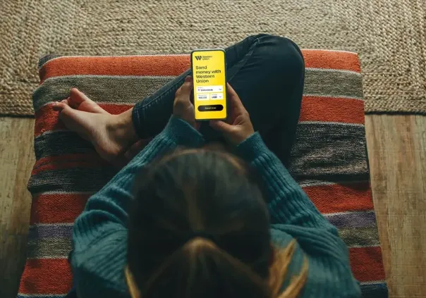 human sitting and holding phone with western union app opened