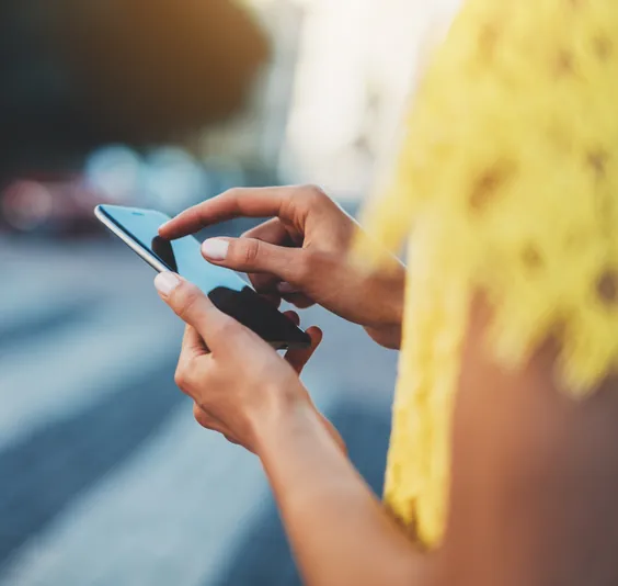 Woman in a yellow shirt uses a mobile phone to check CAD to EUR exchange rates.